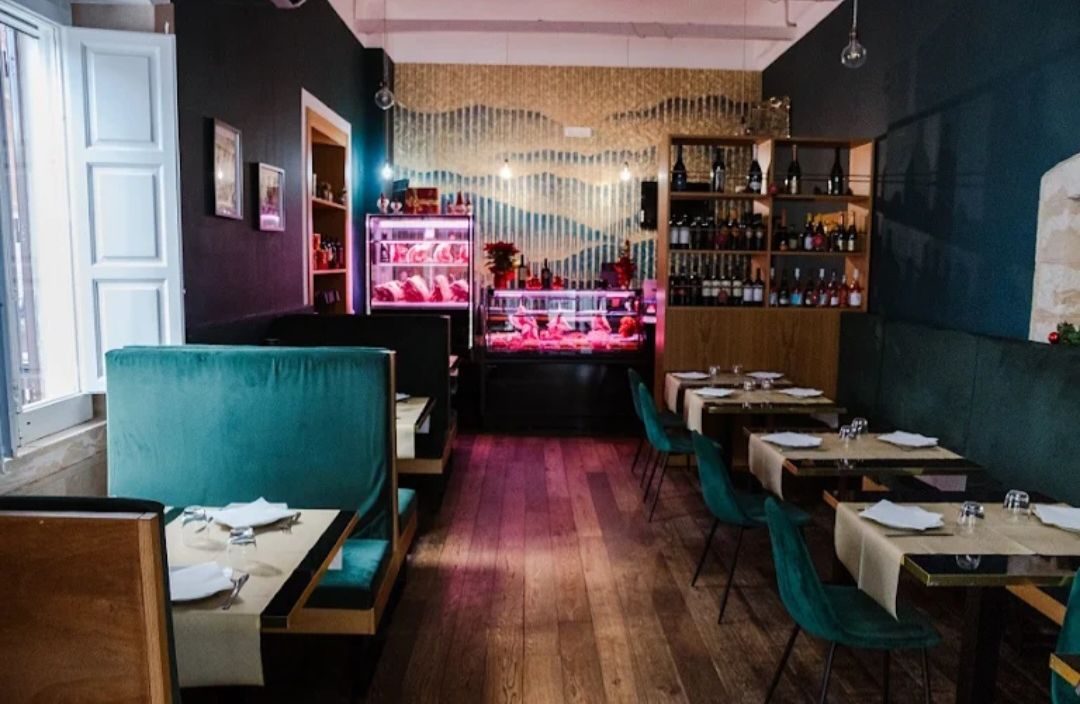 La sala: divanetti in velluto verde, tavoli apparecchiati, vetrina della carne e cantina a vista